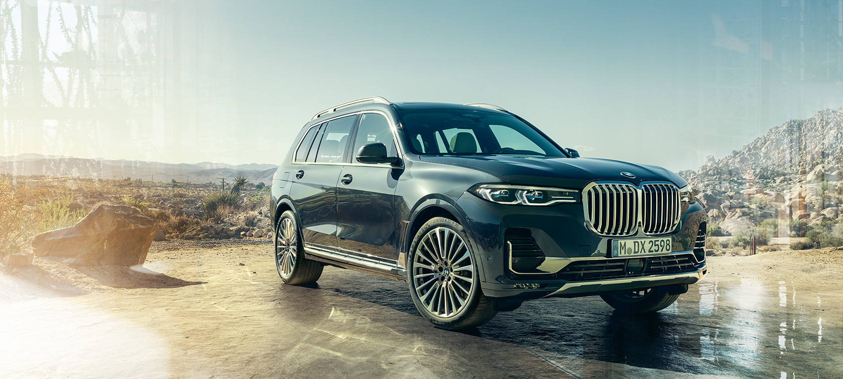 Imagine cu trei sferturi din partea frontală a BMW X7 Imagine cu trei sferturi din partea frontală a BMW X7 în Gri Arctic staţionând în faţa unui deşert, G07 2019