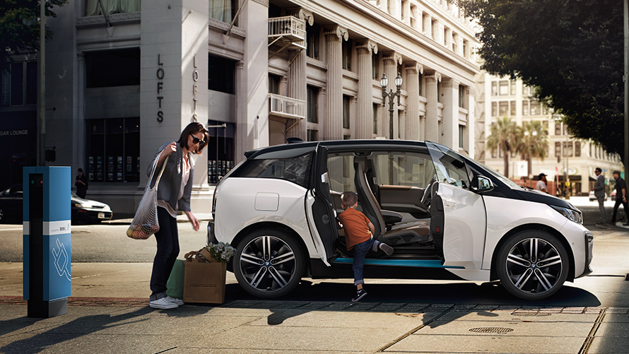 Un BMW i3 în faţa unui peisaj urban Autonomia BMW: un BMW i3 cu o femeie şi un copil în faţa unui peisaj urban