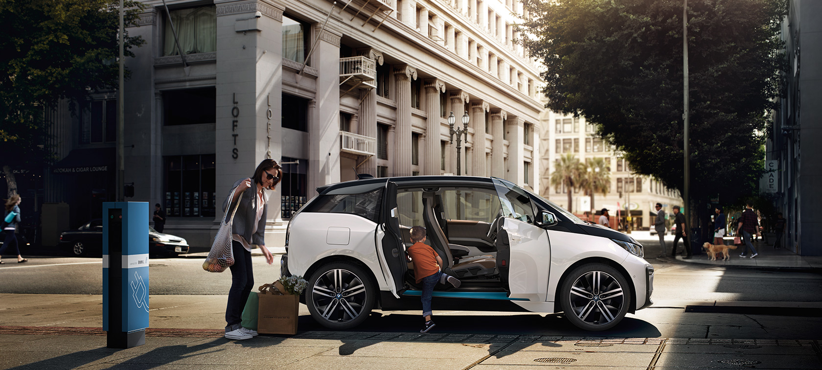 Un BMW i3 în faţa unui peisaj urban Autonomia BMW: un BMW i3 cu o femeie şi un copil în faţa unui peisaj urban