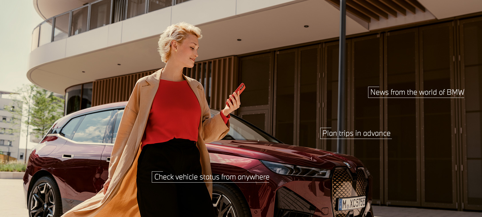 Femeie care stă în faţa unui BMW iX roșu şi foloseşte aplicaţia My BMW pe smartphone Femeie care stă în faţa unui BMW iX roșu şi foloseşte aplicaţia My BMW pe smartphone
