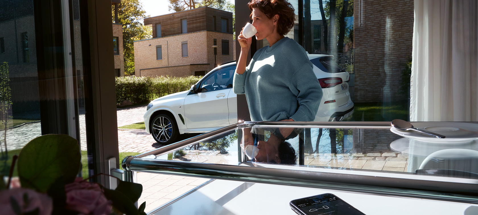 BMW Remote Software Upgrade Femeie care bea dintr-o ceaşcă în timp ce BMW Remote Software Upgrade actualizează software-ul automobilului său BMW X5