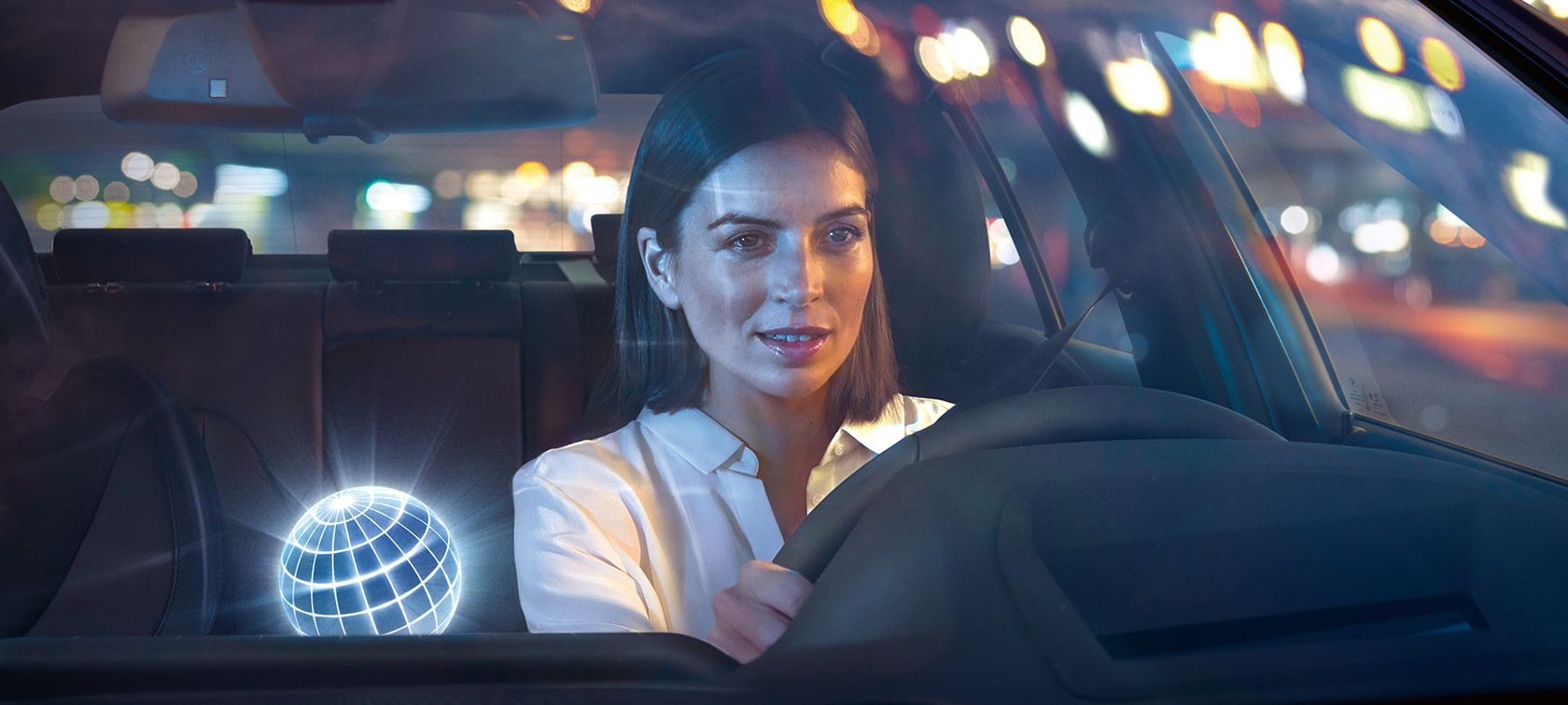 „BMW Intelligent Personal Assistant” O femeie conducând un automobil BMW într-un peisaj nocturn