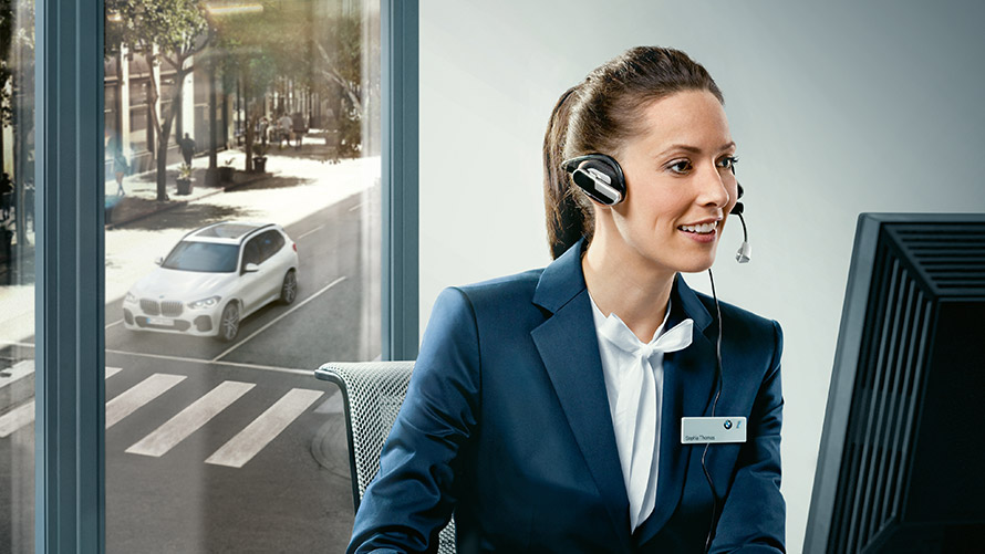 Serviciul de asistenţă „Concierge” Serviciile Concierge: un angajat BMW stând la birou şi purtând căşti