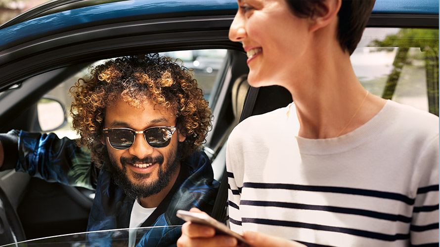 Aplicaţia „BMW Connected” Un bărbat într-un automobil BMW şi o femeie în afara automobilului, folosind aplicaţia „BMW Connected” pe smartphone-urile lor