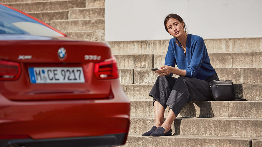 Service şi asistenţă la faţa locului O femeie stând în faţa automobilului său BMW şi folosind funcţia Service şi asistenţă în cazul unei defecţiuni