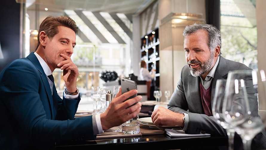 Gestionează locaţiile tale preferate Doi bărbaţi într-un restaurant, folosind pe smartphone funcţia Gestionează locaţiile tale preferate
