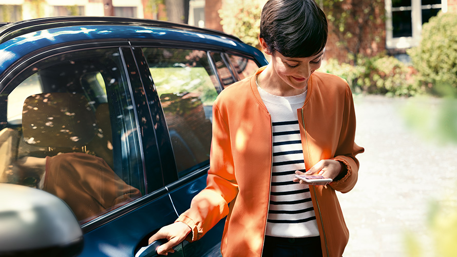 BMW Teleservices Femeie stând cu un smartphone în mână lângă portiera BMW-ului său