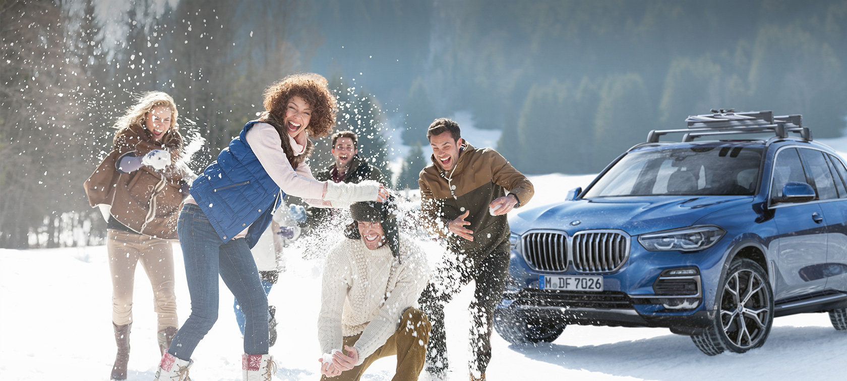 Accesorii originale BMW şi service BMW pentru toamnă şi iarnă Femei şi bărbaţi râzând în zăpadă în faţa unui BMW