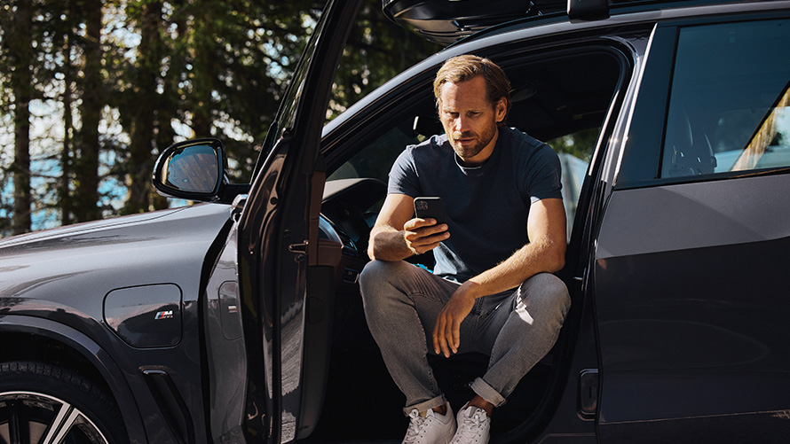 Bărbat care se află într-un BMW şi se uită la smartphone Accesorii pentru primăvară/vară BMW Bărbat care se află într-un BMW şi se uită la smartphone