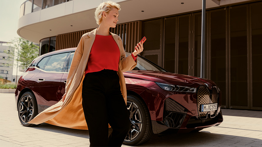 Aplicaţia My BMW Woman with smartphone in front of a BMW