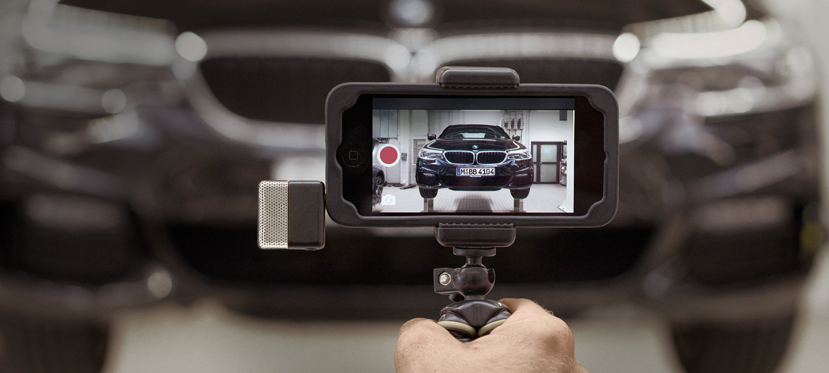 Video service BMW rulând pe smartphone Imagine cu un video Service BMW rulând pe un smartphone în faţa unui BMW
