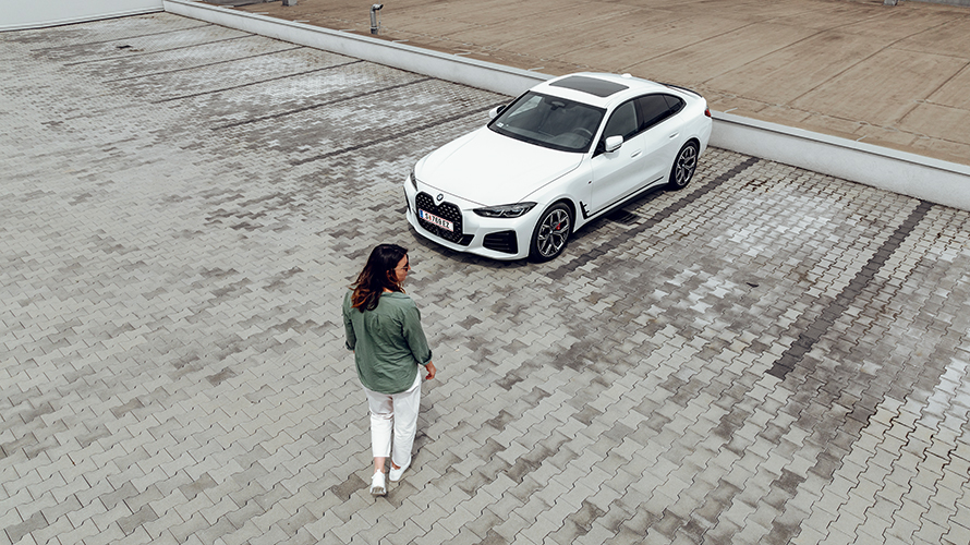 Femeie care merge spre BMW i4, dar priveşte înspre partea dreaptă. Femeie care merge spre BMW i4, dar priveşte înspre partea dreaptă.