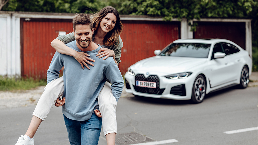 Om care zâmbeşte depărtându-se de BMW i4 şi purtând o femeie care zâmbeşte în spate. Om care zâmbeşte depărtându-se de BMW i4 şi purtând o femeie care zâmbeşte în spate.