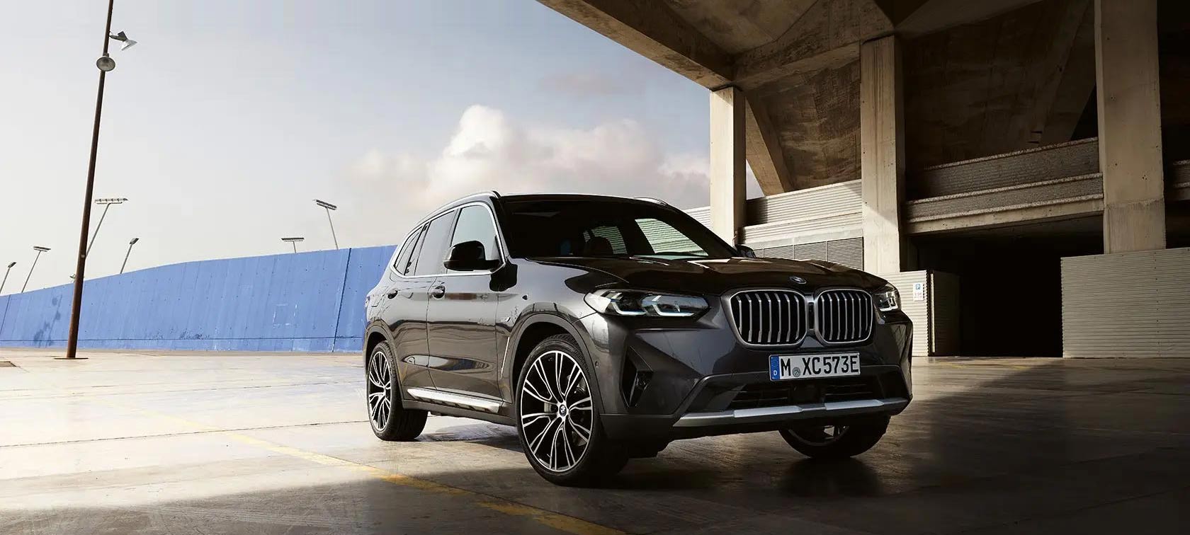 Imagine cu trei sferturi din partea frontală a BMW X3 G01 2021 în Gri Sophisto, în faţa unui hangar