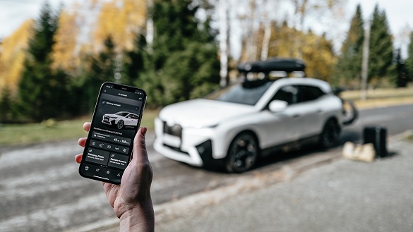 Telefon cu aplicaţia My BMW deschisă şi iX cu accesorii în fundal. Telefon cu aplicaţia My BMW deschisă şi iX cu accesorii în fundal.