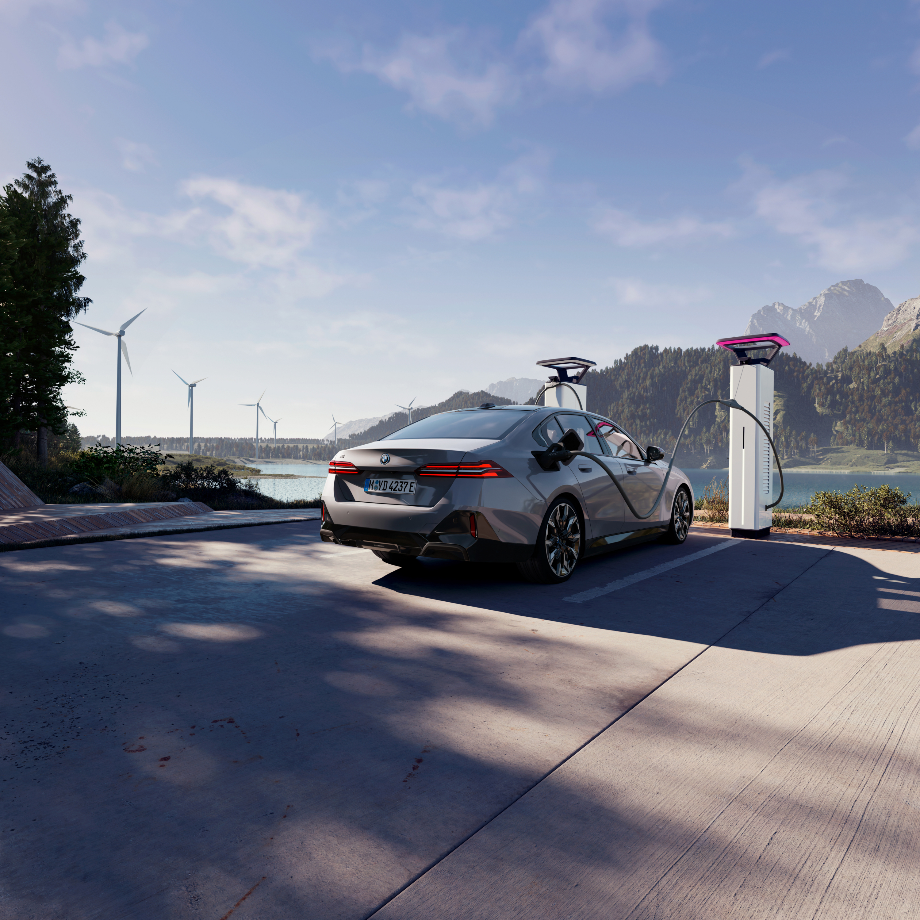 BMW care se încarcă la un stâlp de încărcare cu vedere la apă, munţi şi turbine eoliene