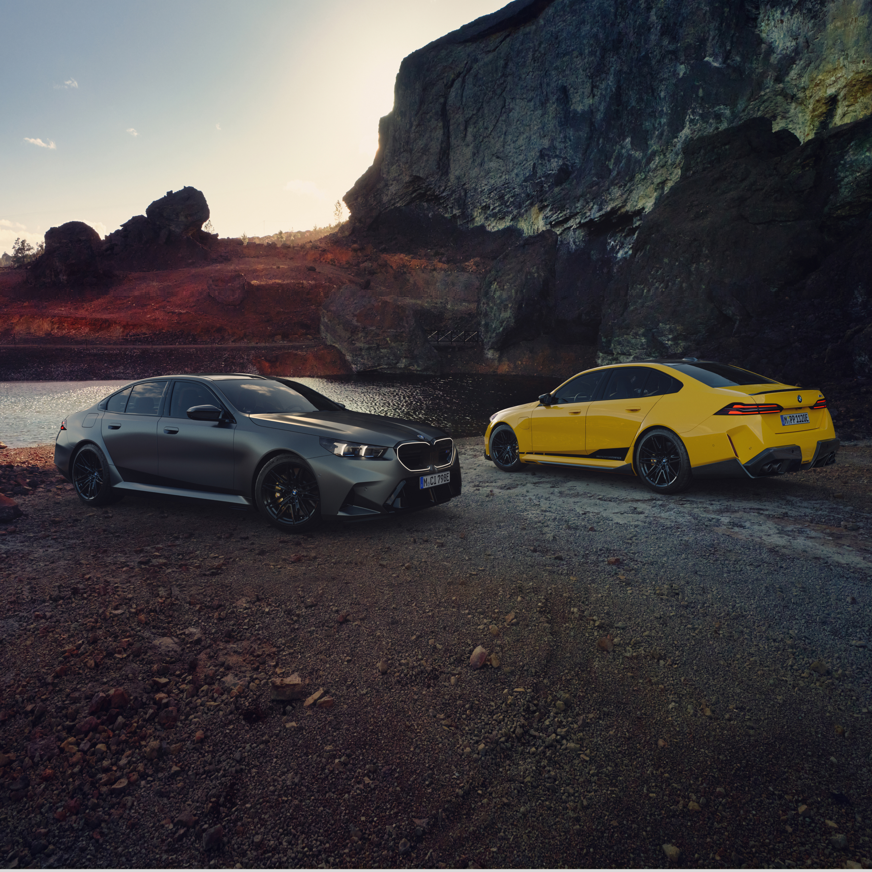 Două modele BMW Seria 5 sunt parcate pe plajă în fața unei stânci